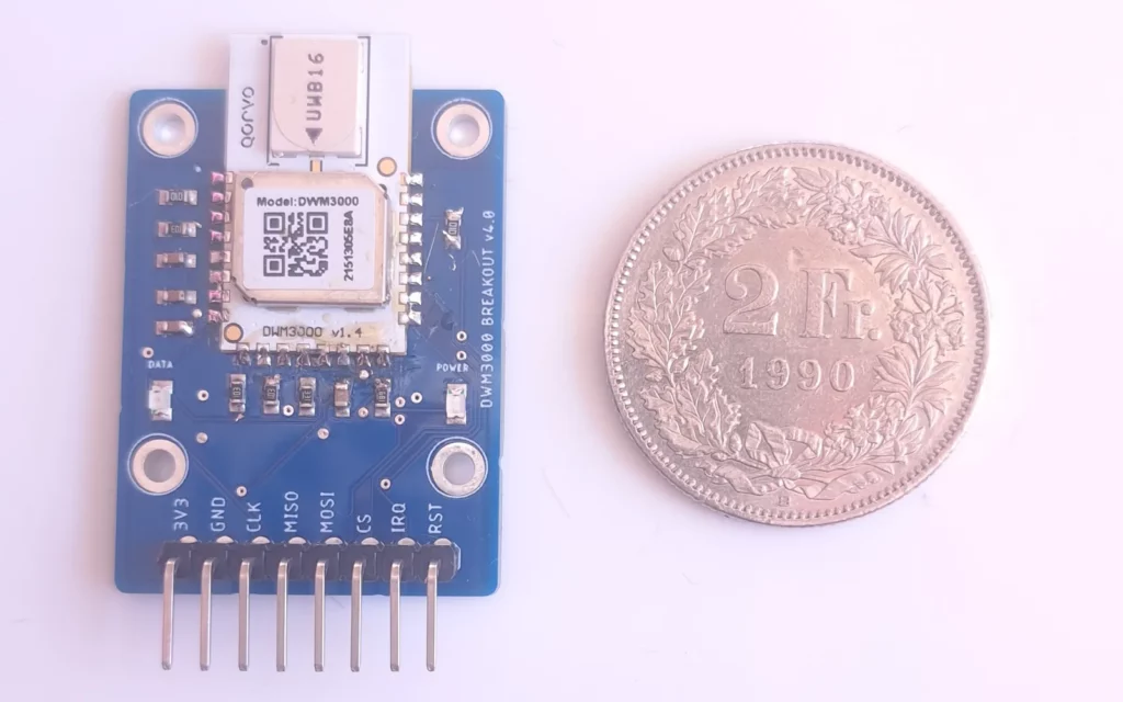 Module UWB DWM3000 sur sa carte d'adaptation bleue, à côté d'une pièce de 2 francs